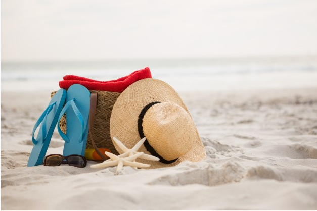 em uma praia estão um par de chinelos junto de uma bolsa e um chapéu perto de uma estrela do mar