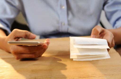 imagem de um homem de camisa azul segurando suas contas e usando seu celular