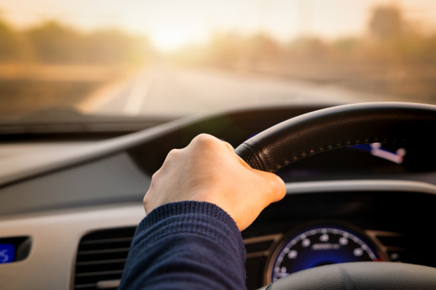 imagem ampliada de mão de pessoa segurando o volante de um automóvel dirigindo por uma estrada