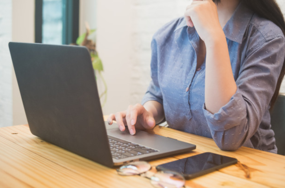 imagem ampliada de uma mulher de camisa azul trabalhando em frente ao seu laptop sentada a uma mesa de madeira