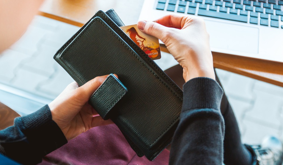 imagem em close de uma carteira na qual uma mulher retira um cartão de crédito