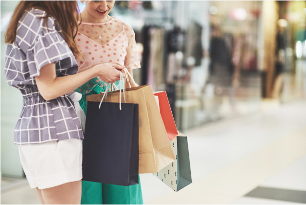 duas mulheres dentro de shopping conversam enquanto seguram sacolas de compras