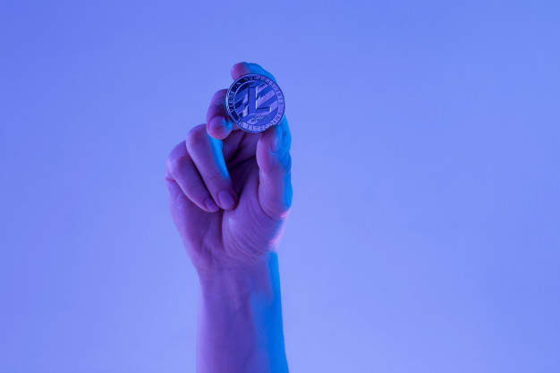mão segurando moeda com símbolo do Litecoin em um lugar azul