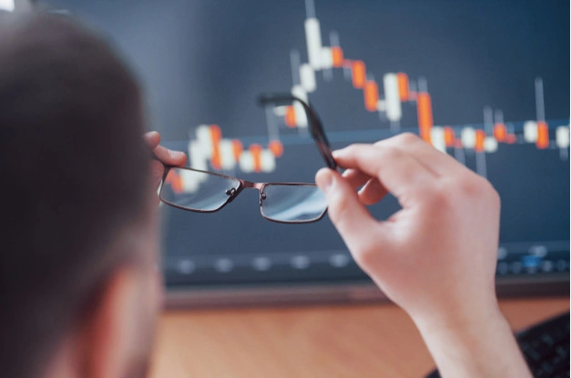 imagem ampliada de uma tela com gráfico de investimentos em frente a  um homem posicionando seus óculos