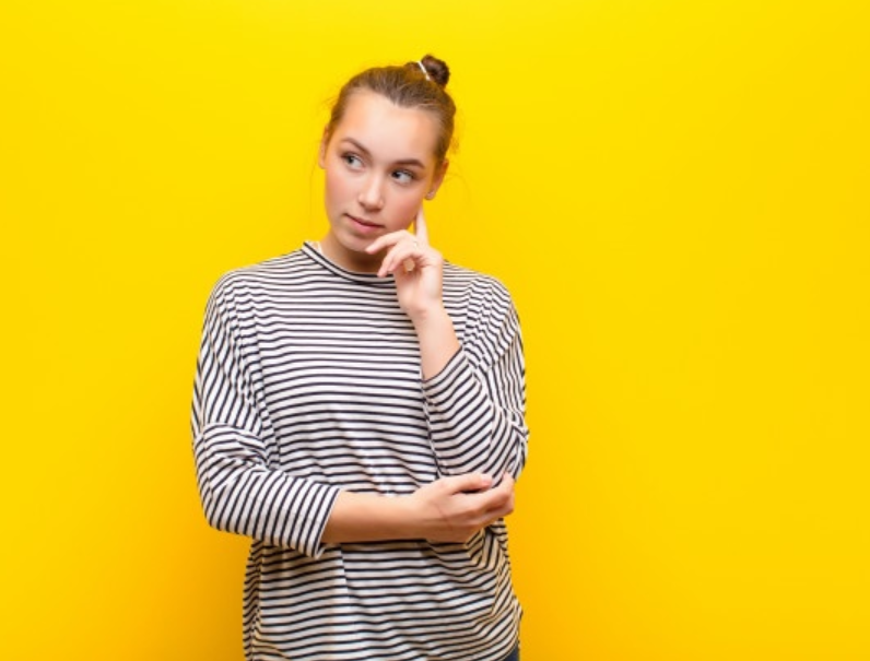 imagem de garota loira com camiseta listrada pensativa em frente a uma parede amarela